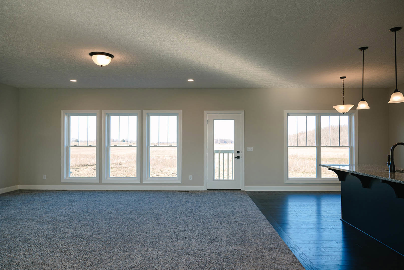 Bright dining area with large windows overlooking a grassy field, marble-topped table, white walls, carpeted floor, and dark trim accents.