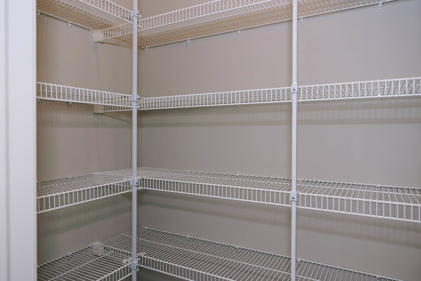 White wire shelving mounted on a grey wall in a room, featuring metal bars and open storage design.