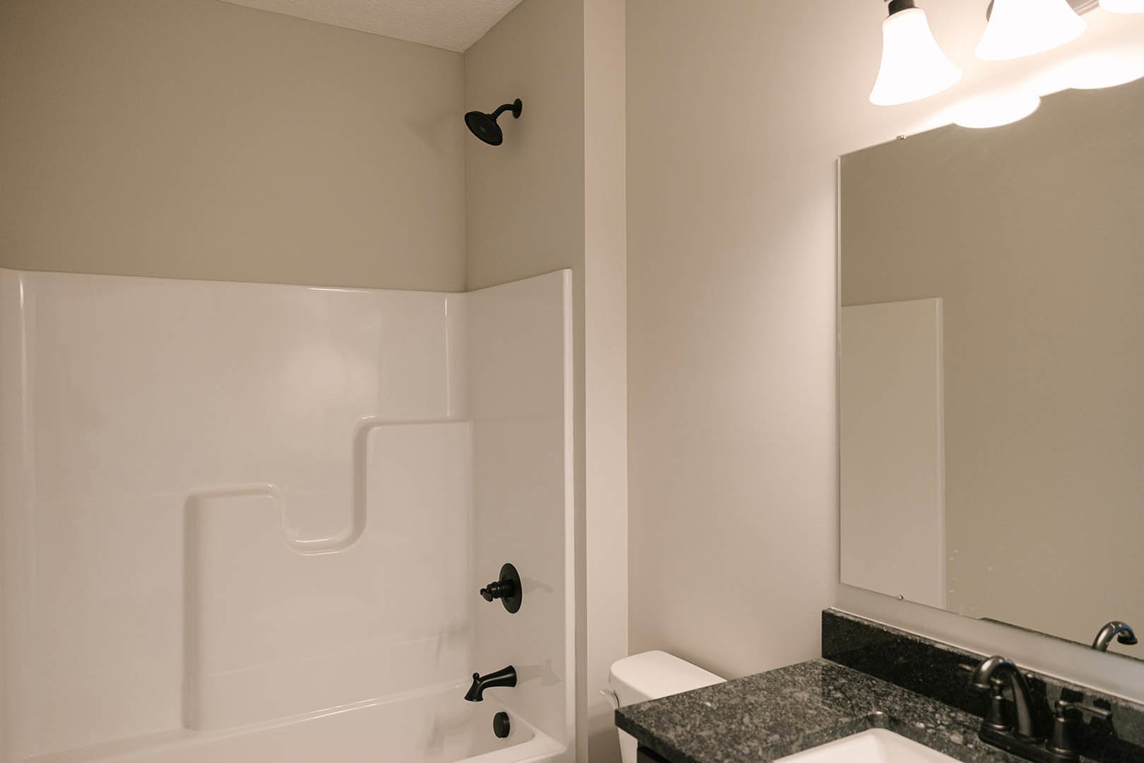Bathroom with white bathtub and black faucets, black countertop with matching black sink and shower fixtures, tile walls, and ceiling light.