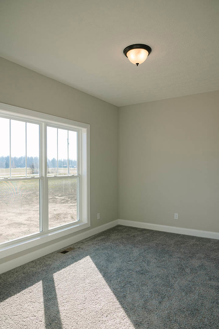 Carpeted bedroom with white plaster walls, large window featuring cracked glass, and ceiling-mounted light fixture