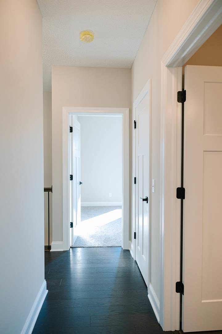 Hallway with dark wood flooring, white paneled doors, white walls, and brushed metal door handles