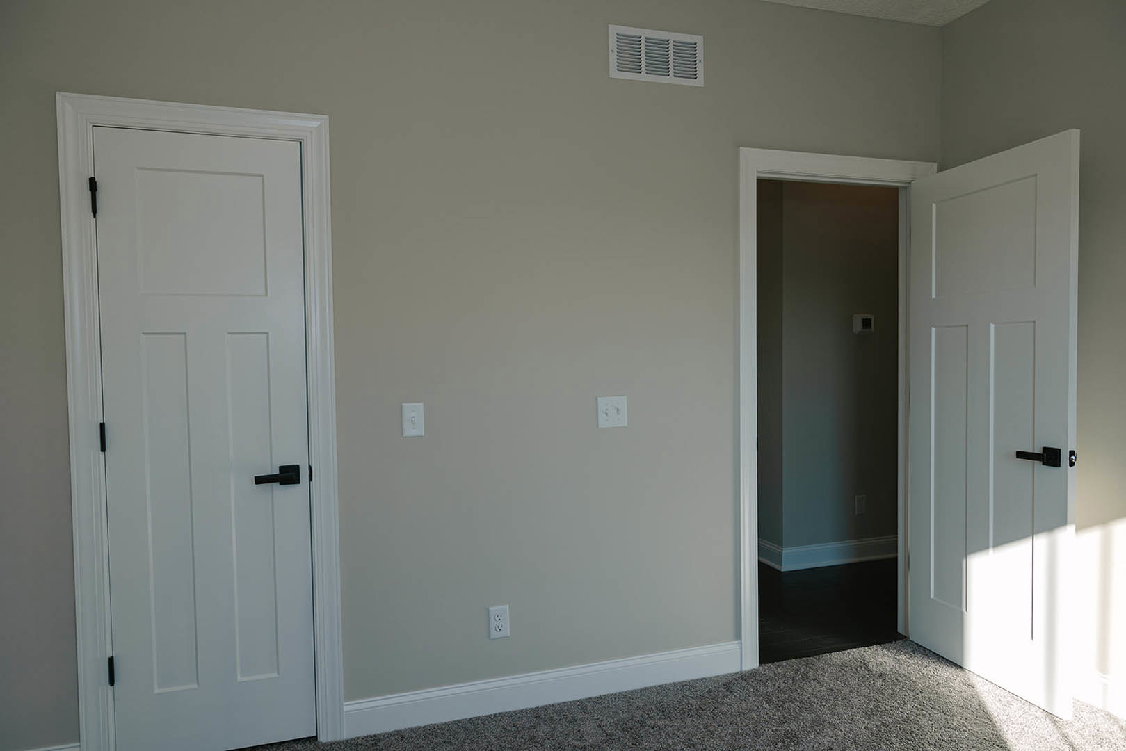 White paneled door with black handle open to a room, white walls, ceiling vent, light switch, and wood flooring visible