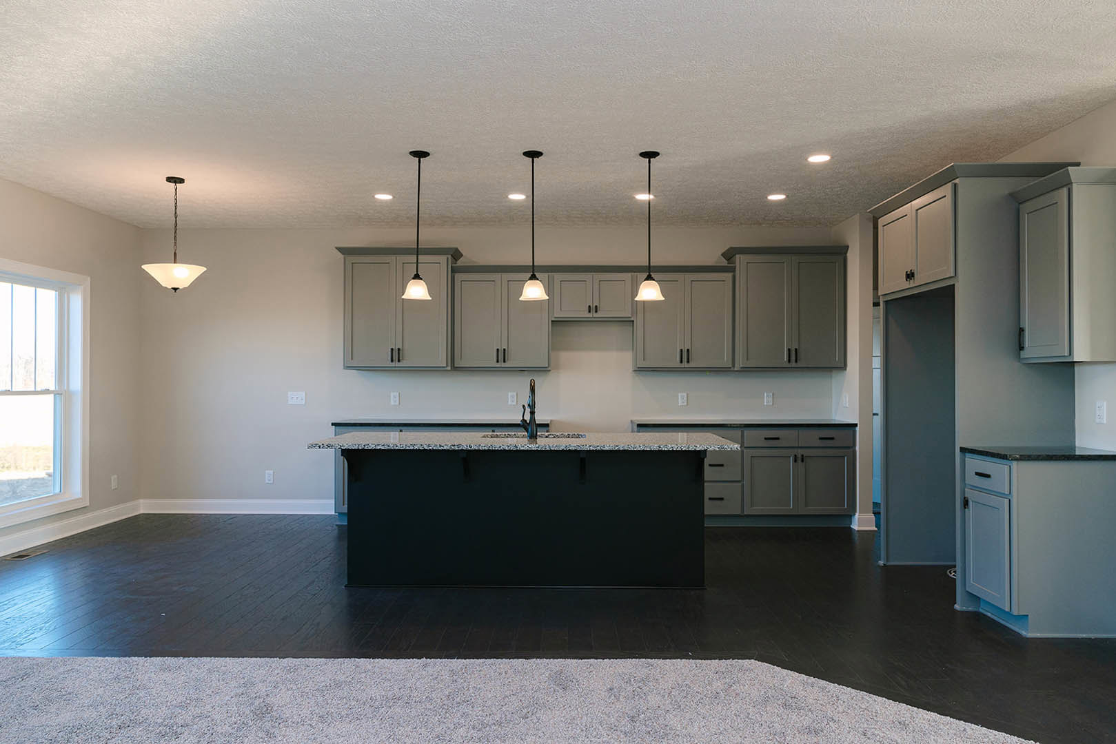 Modern kitchen featuring a central island with white cabinetry and black handles, stone countertop with built-in sink, pendant light fixture suspended from chain, door leading