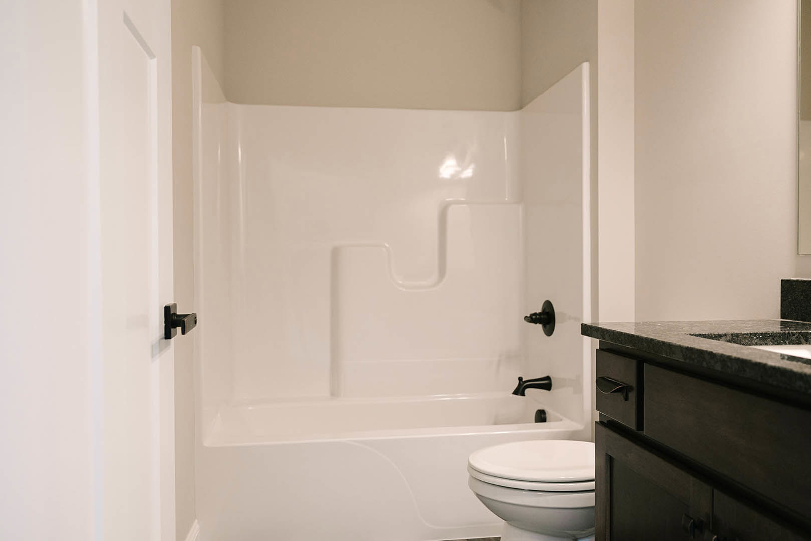 Freestanding white bathtub beside matching toilet, light gray tile flooring, white walls, chrome faucet, and modern vanity with integrated sink