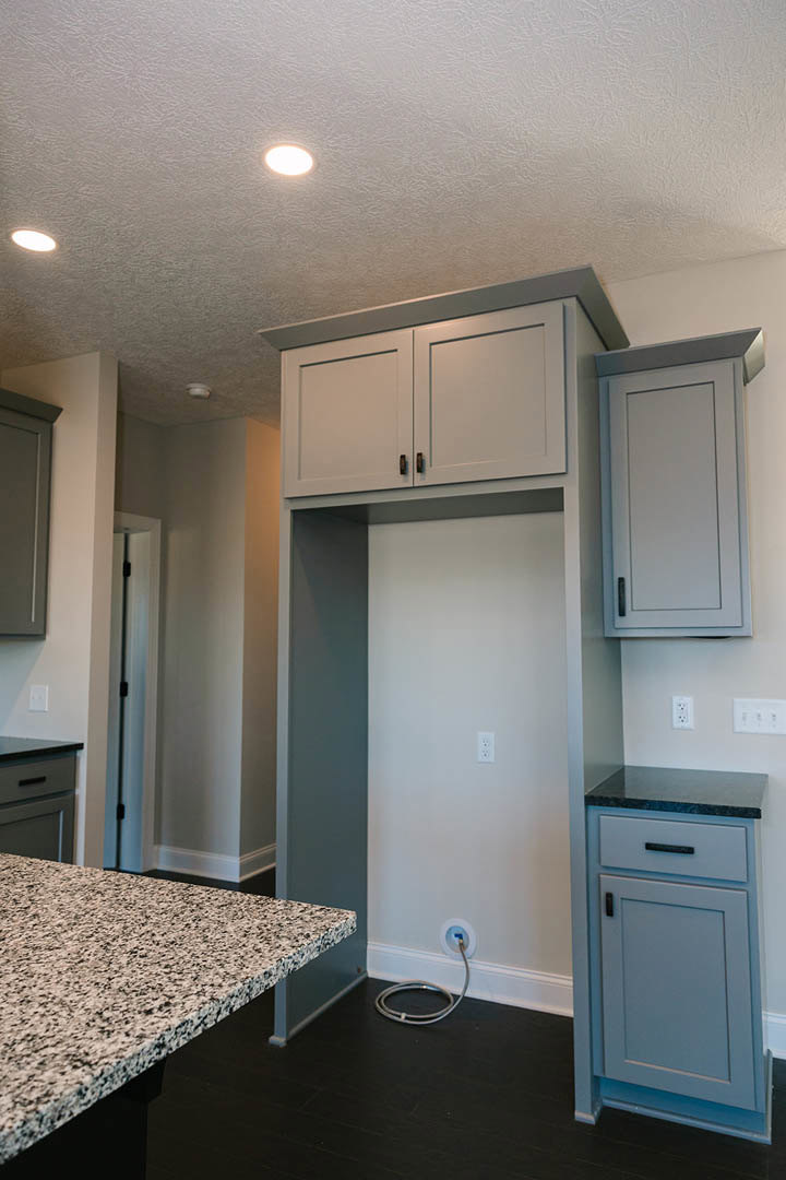 Modern kitchen featuring white shaker cabinets, light stone countertops, stainless steel sink, and blue-bordered door against white walls; visible cable plugged into wall near