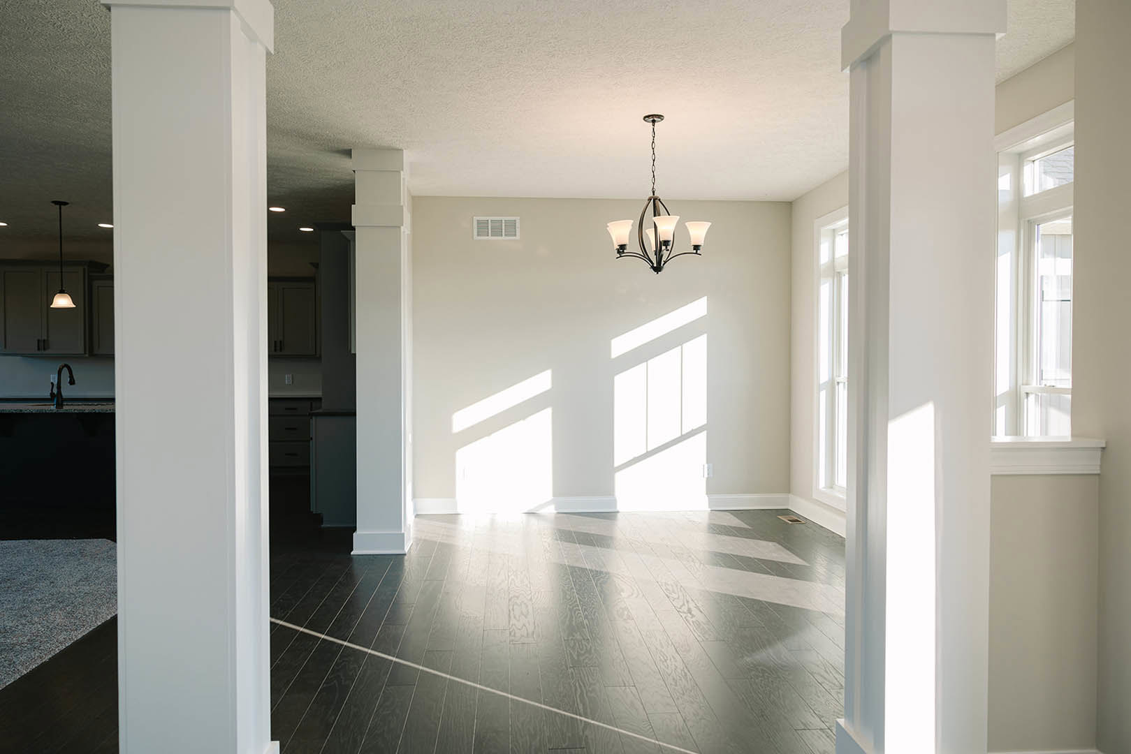 Chandelier hanging from white ceiling above dark hardwood flooring, white pillar in foreground, black faucet with blue handle near textured wall.
