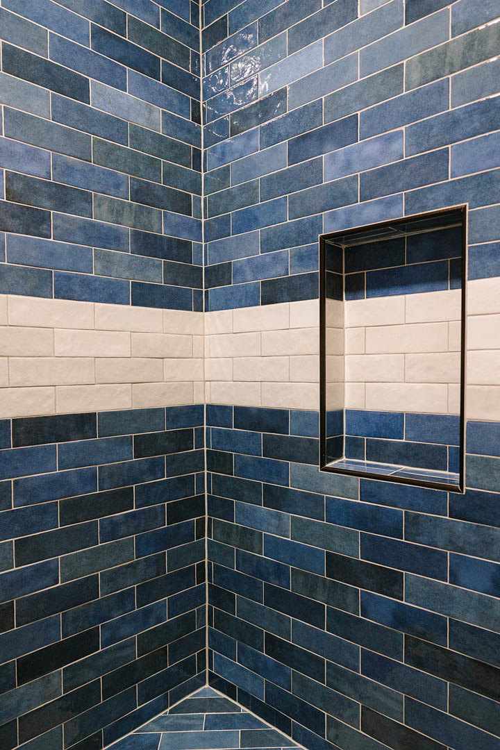 Shower with rectangular built-in shelf, black wall tile, and blue tile floor