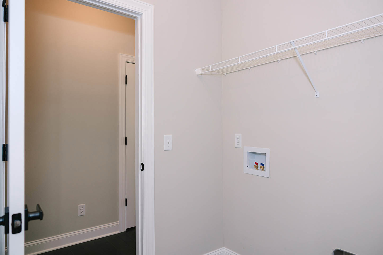 White built-in shelf against a smooth plaster wall in a bathroom, with a door and chrome handle visible, light-colored floor and ceiling, and a mirror reflecting part of the