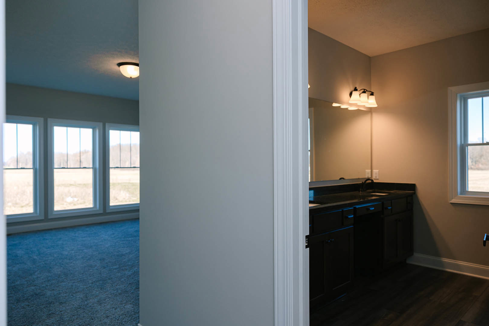 Bathroom featuring a wide mirror above a black countertop with drawers, large window offering outdoor views, light-colored flooring, and modern cabinetry.