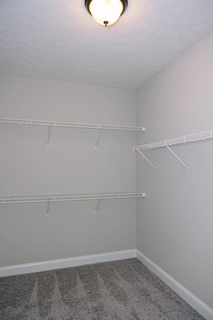 Shelving units line the walls of a room with a carpeted ceiling, white shelves with metal bars, and a ceiling fixture.