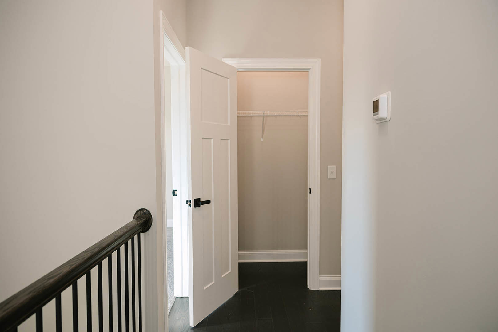 White interior door with black handle open to a room, black metal railing visible beside white plaster wall, dark flooring contrasts with light finishes.