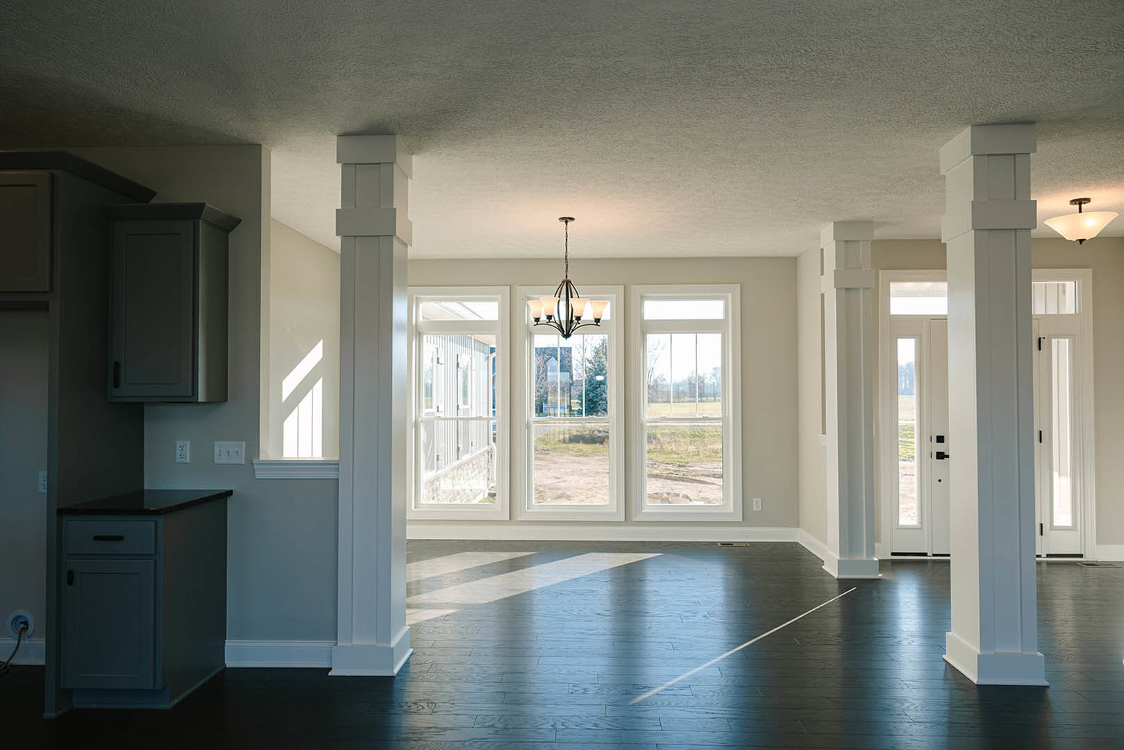Black tile floor and white plaster walls in a modern room, featuring a contemporary chandelier, sleek cabinetry, large window overlooking a grassy field, and a close-up of a wooden