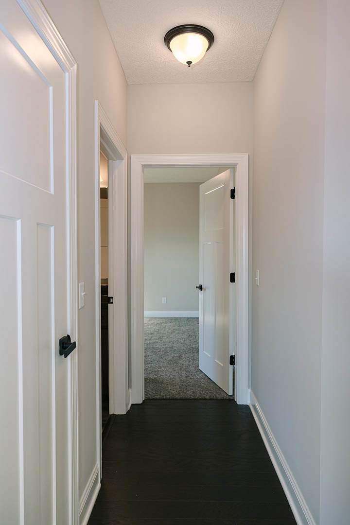 Hallway with white paneled doors, black floor with white baseboard trim, ceiling light fixture, white doors featuring black handles