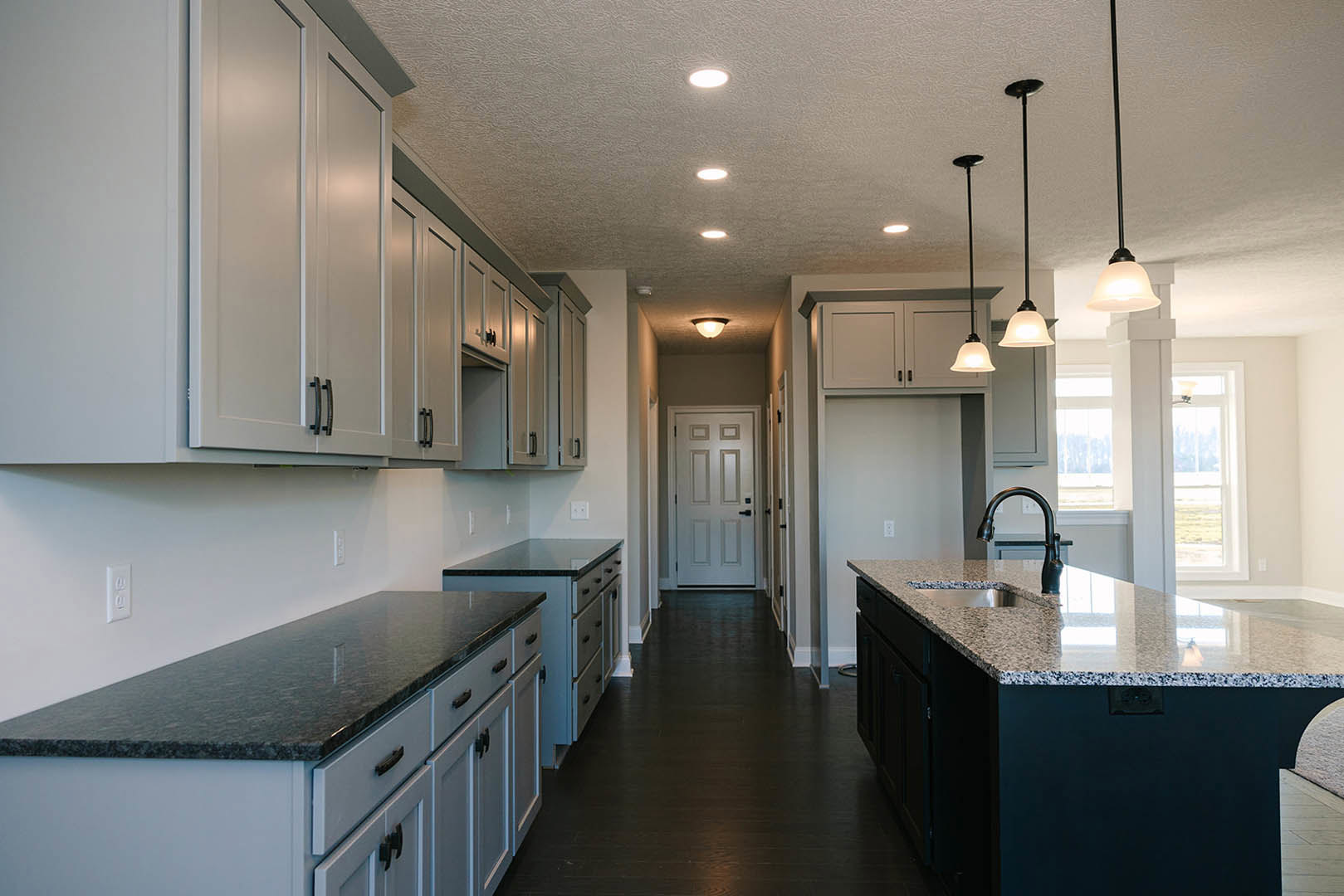 Modern kitchen featuring matte black cabinets and countertop, central island with stainless steel sink and chrome faucet, white door with black handle, white upper cabinetry, light