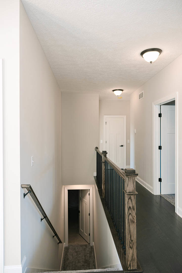 Hallway with white plaster walls, wood flooring, staircase with metal handrail, white door featuring a blue accent line, ceiling light fixture
