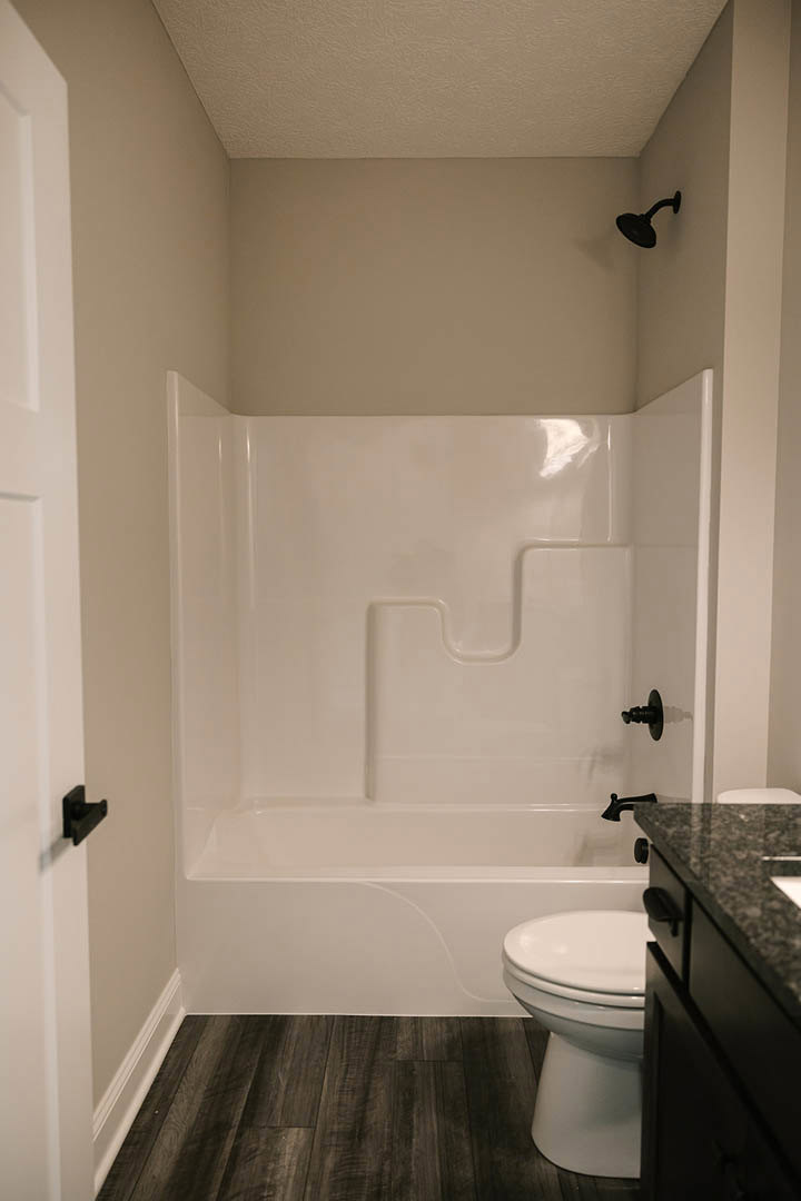 Bathroom with dark wood flooring, white walls, white bathtub with black faucet, black light fixture, white toilet, and close-up of countertop.