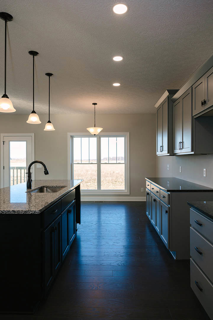 Spacious kitchen featuring a large central island with built-in sink, white cabinetry, dark hardwood flooring, stainless steel appliances, and a window providing natural light
