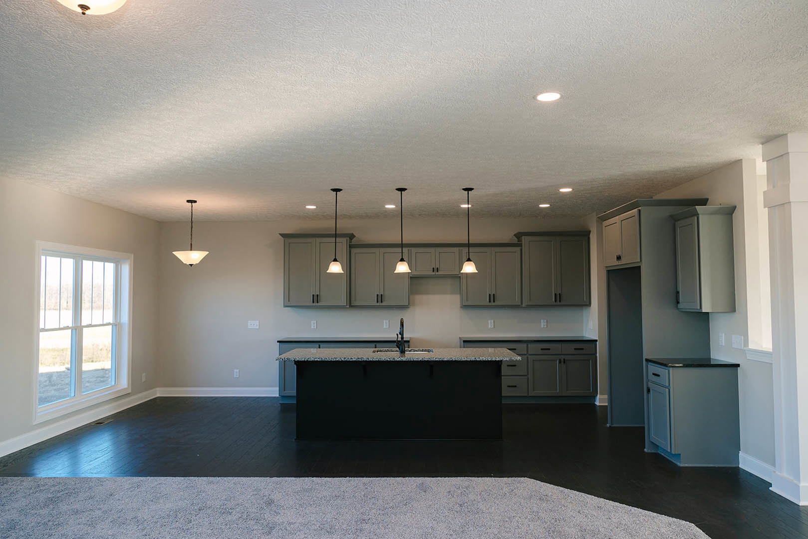 Spacious kitchen featuring a large white island with black countertops, built-in sink, white cabinetry, and a long black pendant wire hanging from the ceiling.