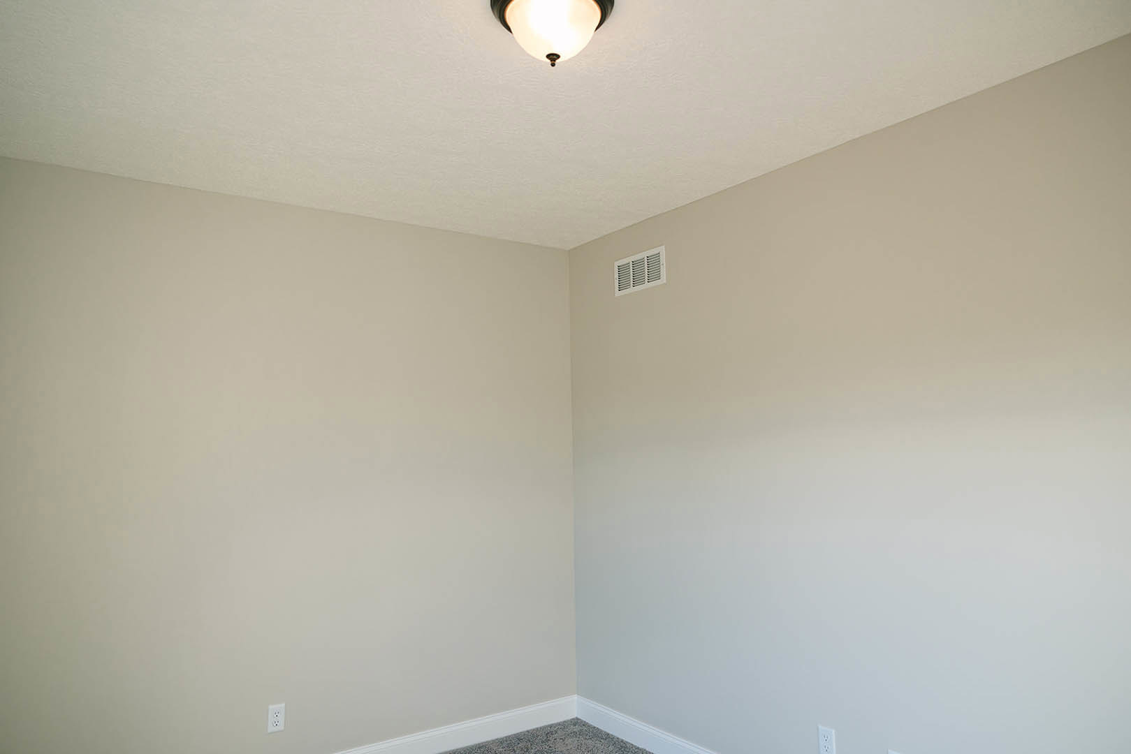 Close-up of a modern ceiling light fixture with white plaster walls, textured carpet flooring, and a vent on the wall in a contemporary room.