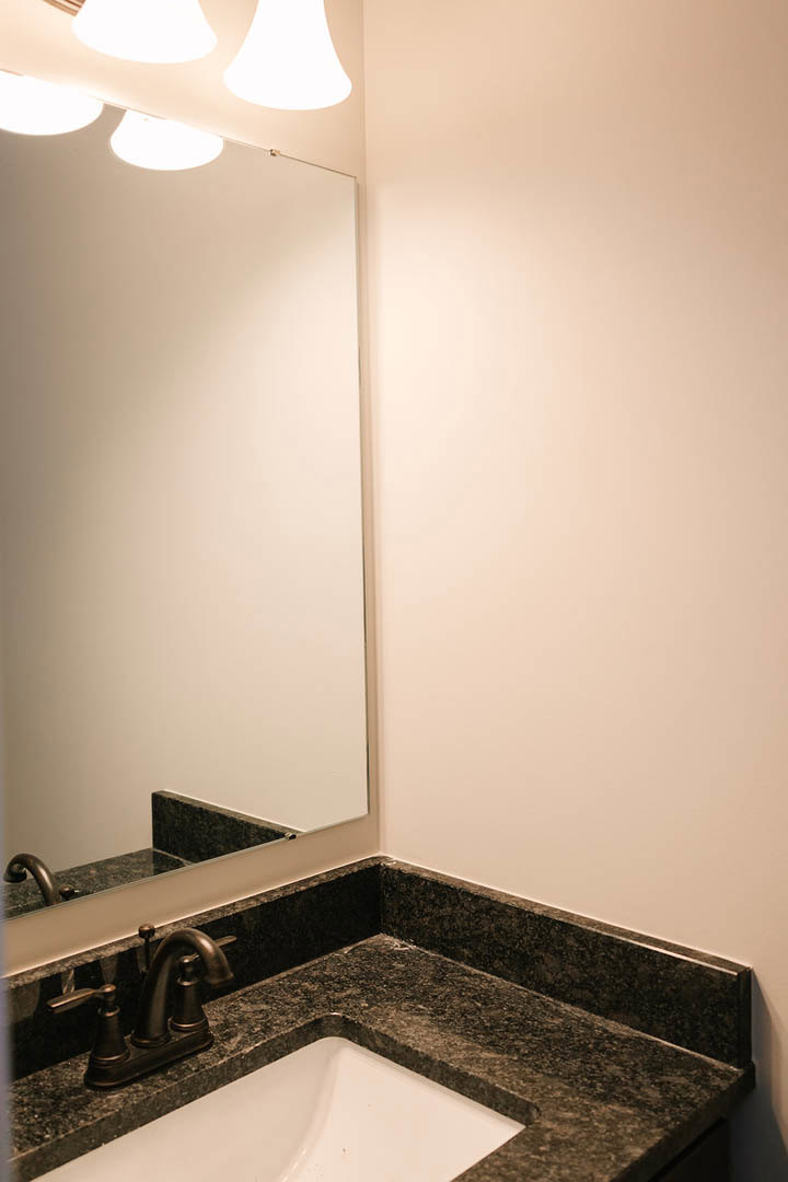White bathroom vanity with rectangular sink, chrome faucet, large frameless mirror, wall-mounted light fixture, and glossy tile backsplash