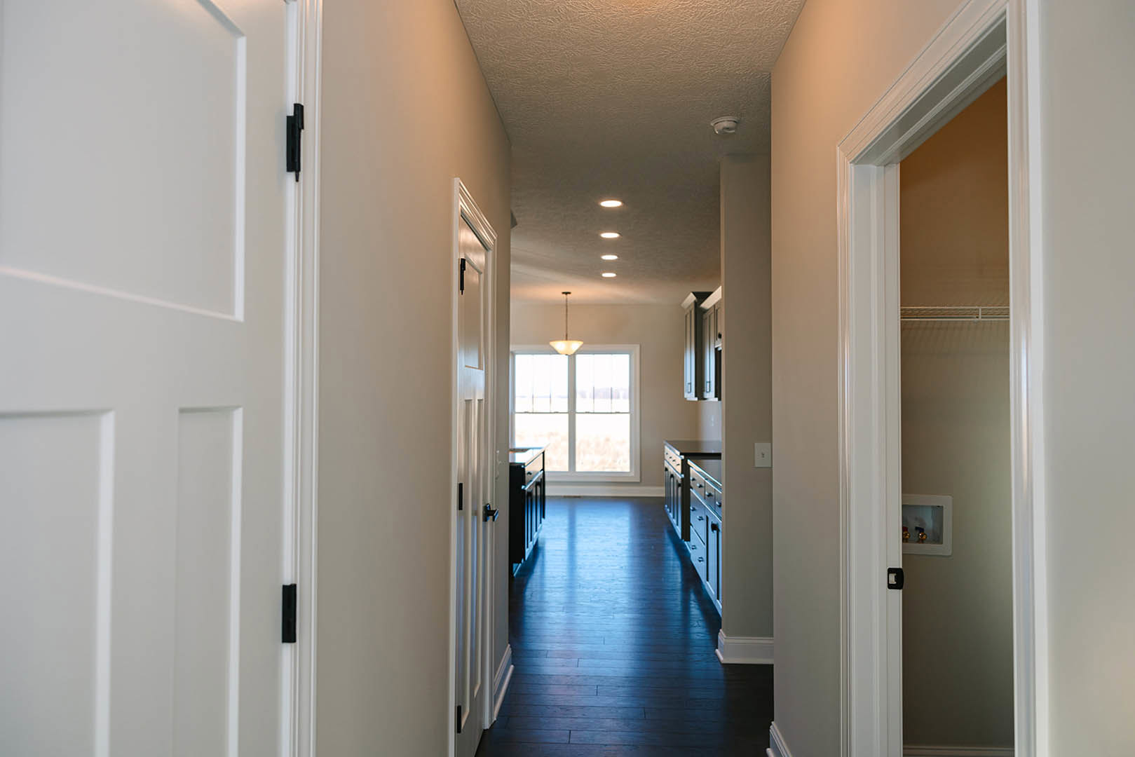 Hallway featuring dark hardwood flooring, white doors and trim, ceiling light fixture, closet with white frame, window, and desk visible in adjacent room