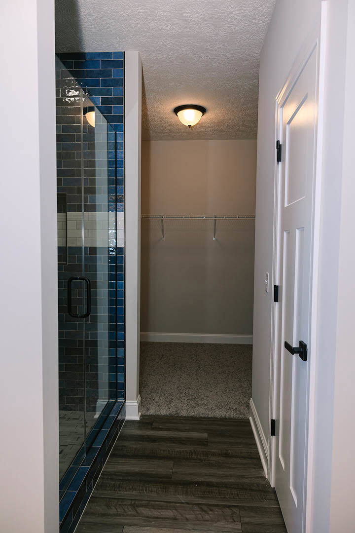 Bathroom with glass shower door and chrome handle, dark wood flooring, marble countertop, ceiling light fixture, built-in shelf, and neutral plaster walls.