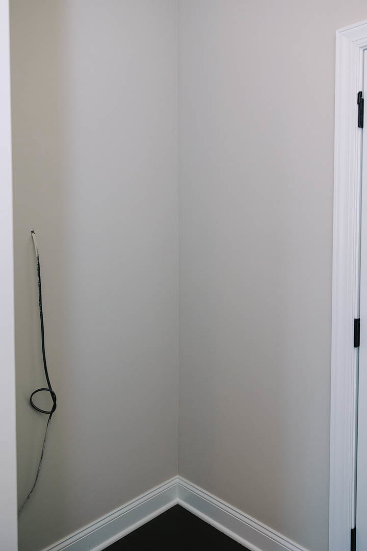 White plaster walls meet at a corner with a black wire running along the surface, adjacent to a white door and light-colored flooring.