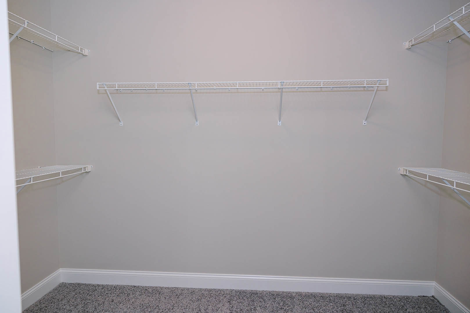 White wall-mounted shelf with metal support bars in a bathroom, plaster walls and ceiling visible in background.