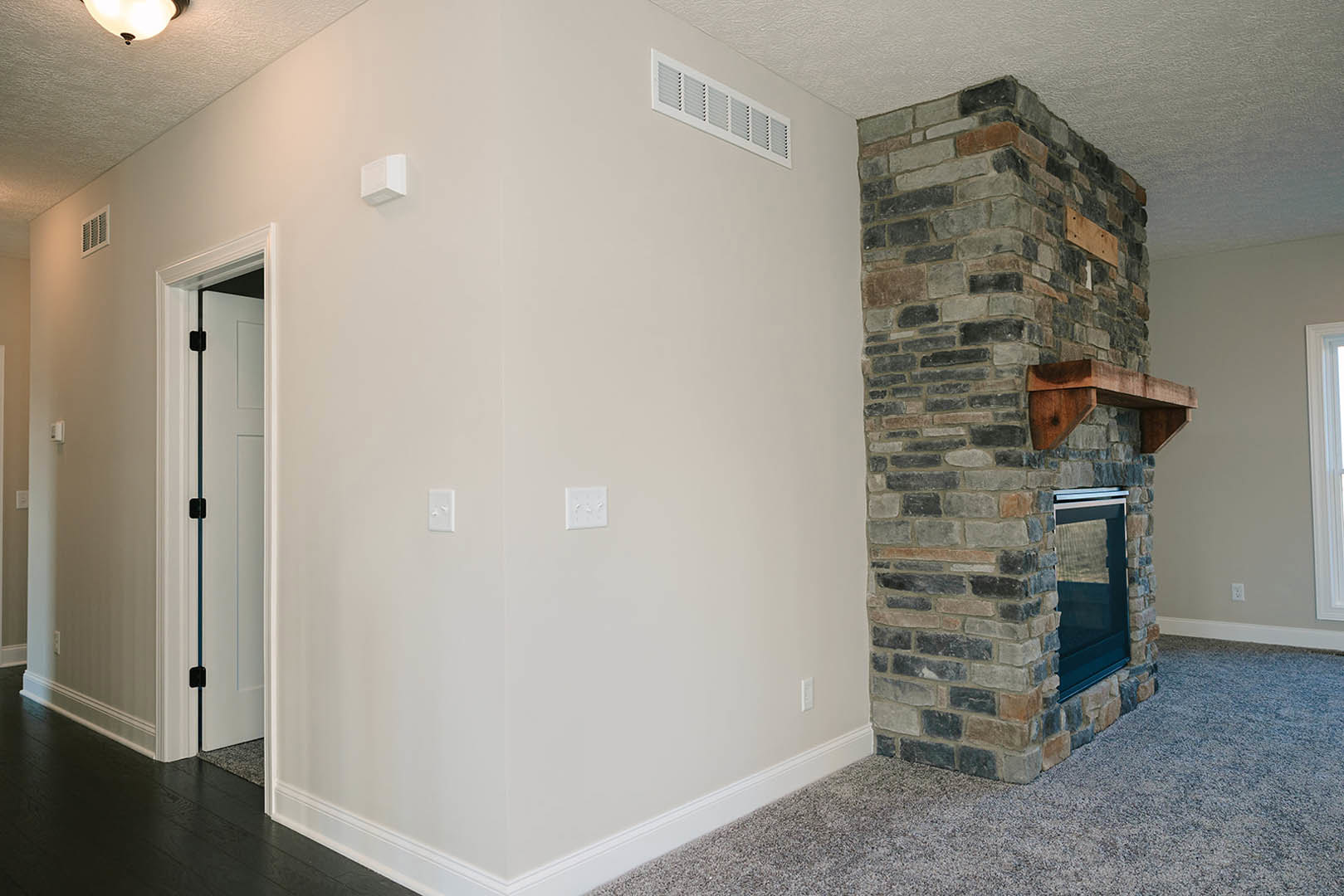 Modern plaster fireplace with wood mantel, white vent above, light hardwood flooring, white walls, and adjacent door in residential living room.