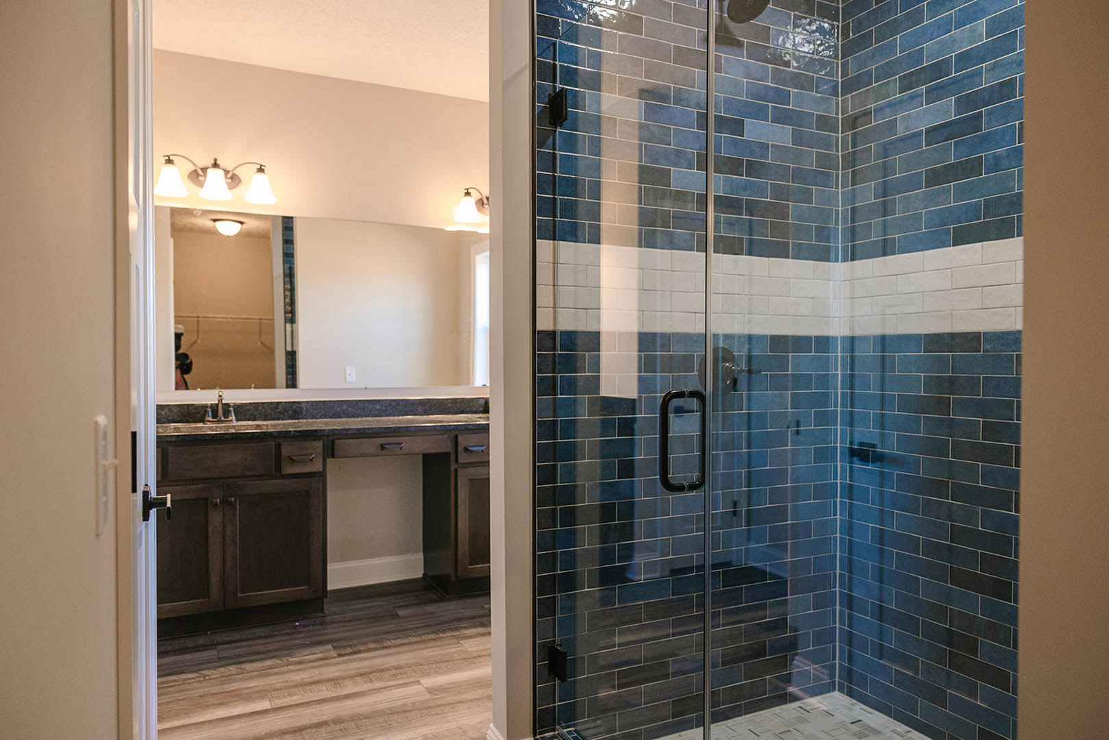 Bathroom featuring a glass-enclosed shower, white sink with chrome faucet, dark wood flooring, white walls, and a wall-mounted light fixture