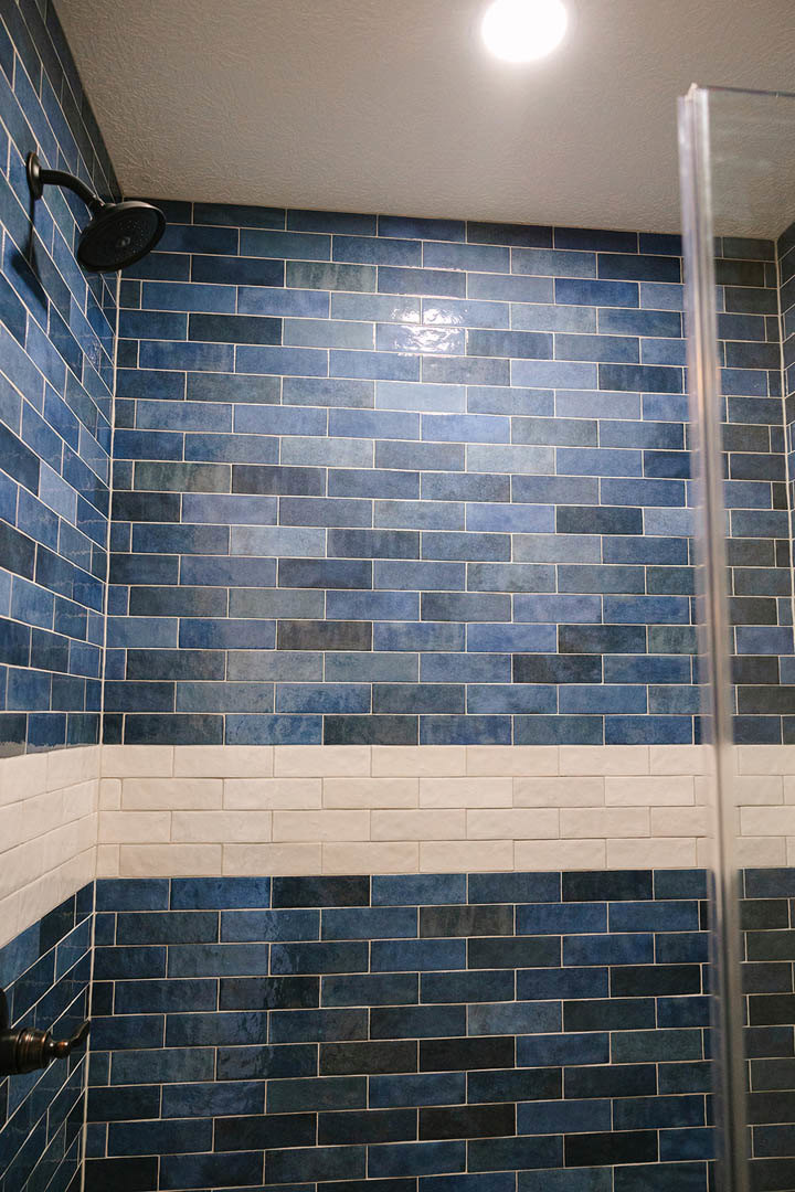 Blue and white tiled shower with chrome showerhead, partial view of shower curtain, and white ceiling
