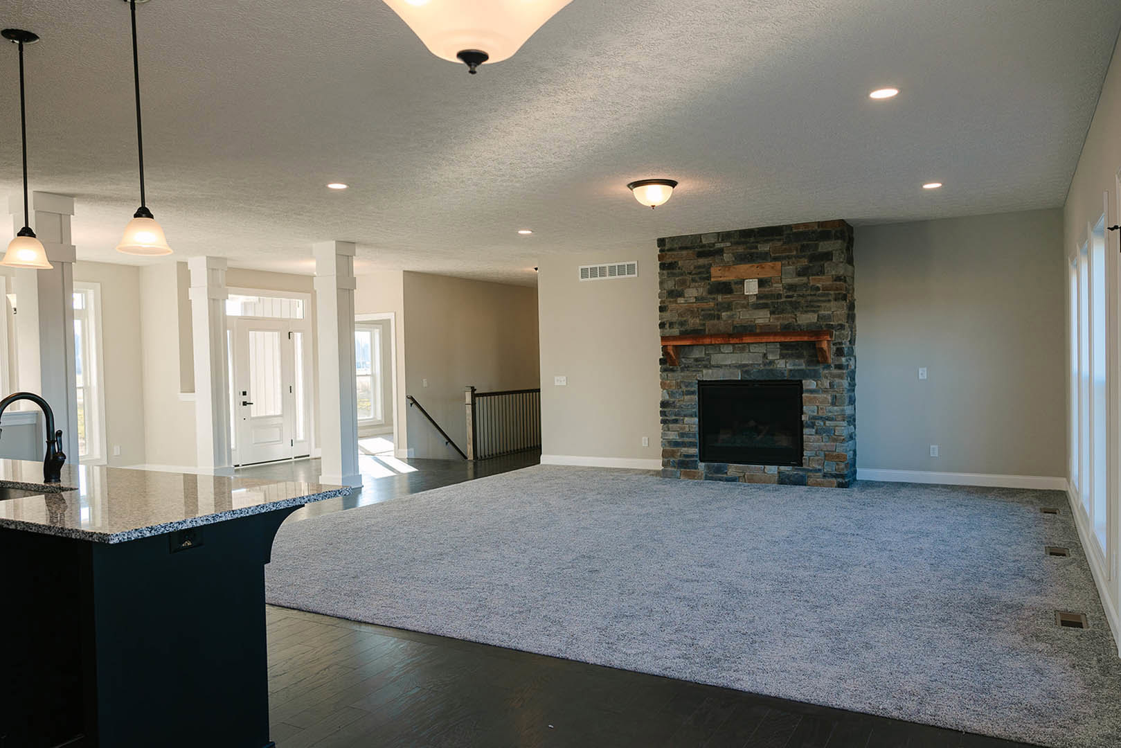 Living room featuring a marble kitchen island, built-in fireplace with wood mantel, light carpet flooring, white plaster walls, and recessed ceiling lighting.