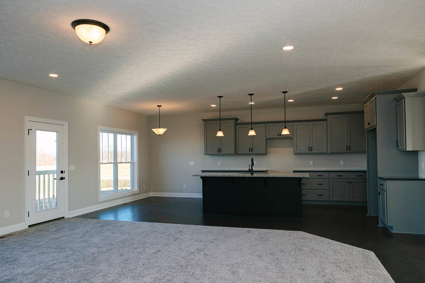 Open-concept kitchen and living room featuring a large central island with stone countertop, white cabinetry, stainless steel sink, wood flooring, ceiling light fixture, and a