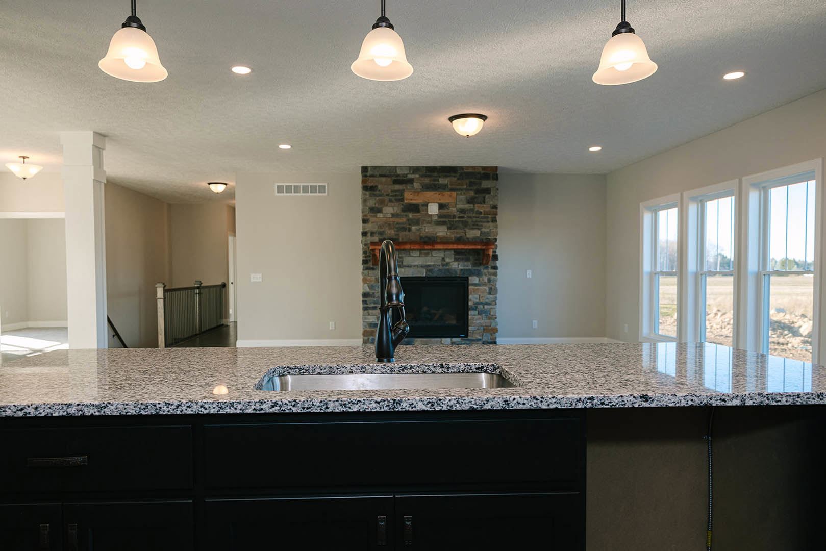 Open kitchen with marble countertop, stainless steel sink, white cabinetry, built-in fireplace, large windows, and modern ceiling light fixture
