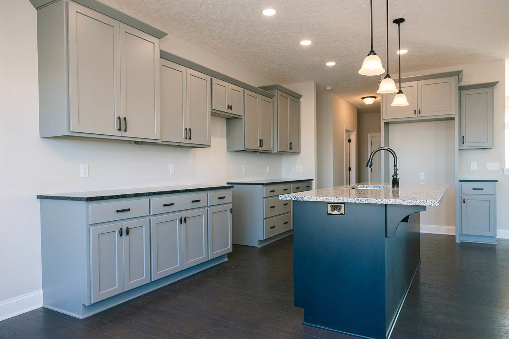 Spacious kitchen featuring a central island with marble countertop, white cabinetry with silver handles, stainless steel faucet, modern pendant light fixture, and white door with