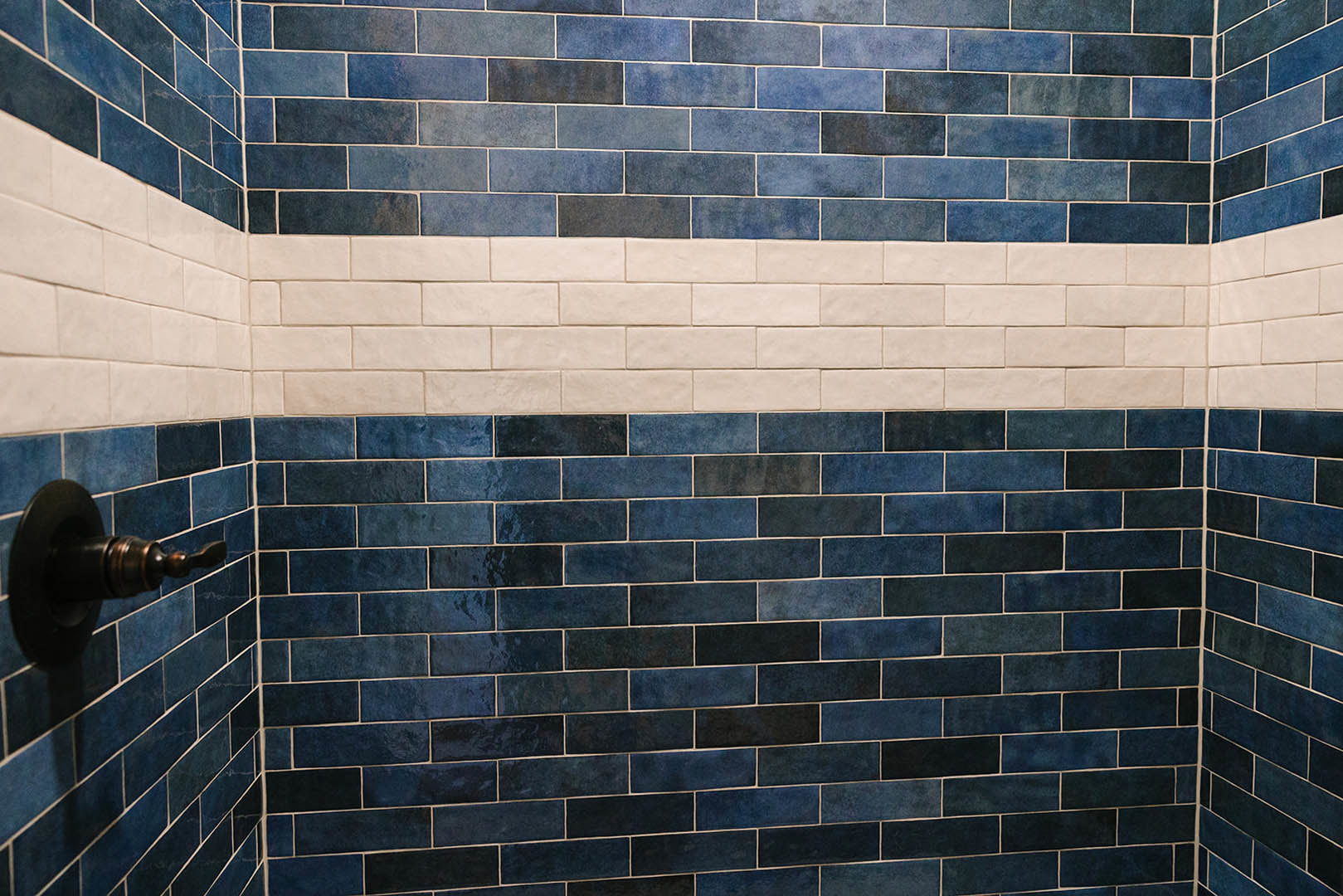 Blue and white tiled bathroom wall with a close-up of a chrome knob and a black rectangular fixture