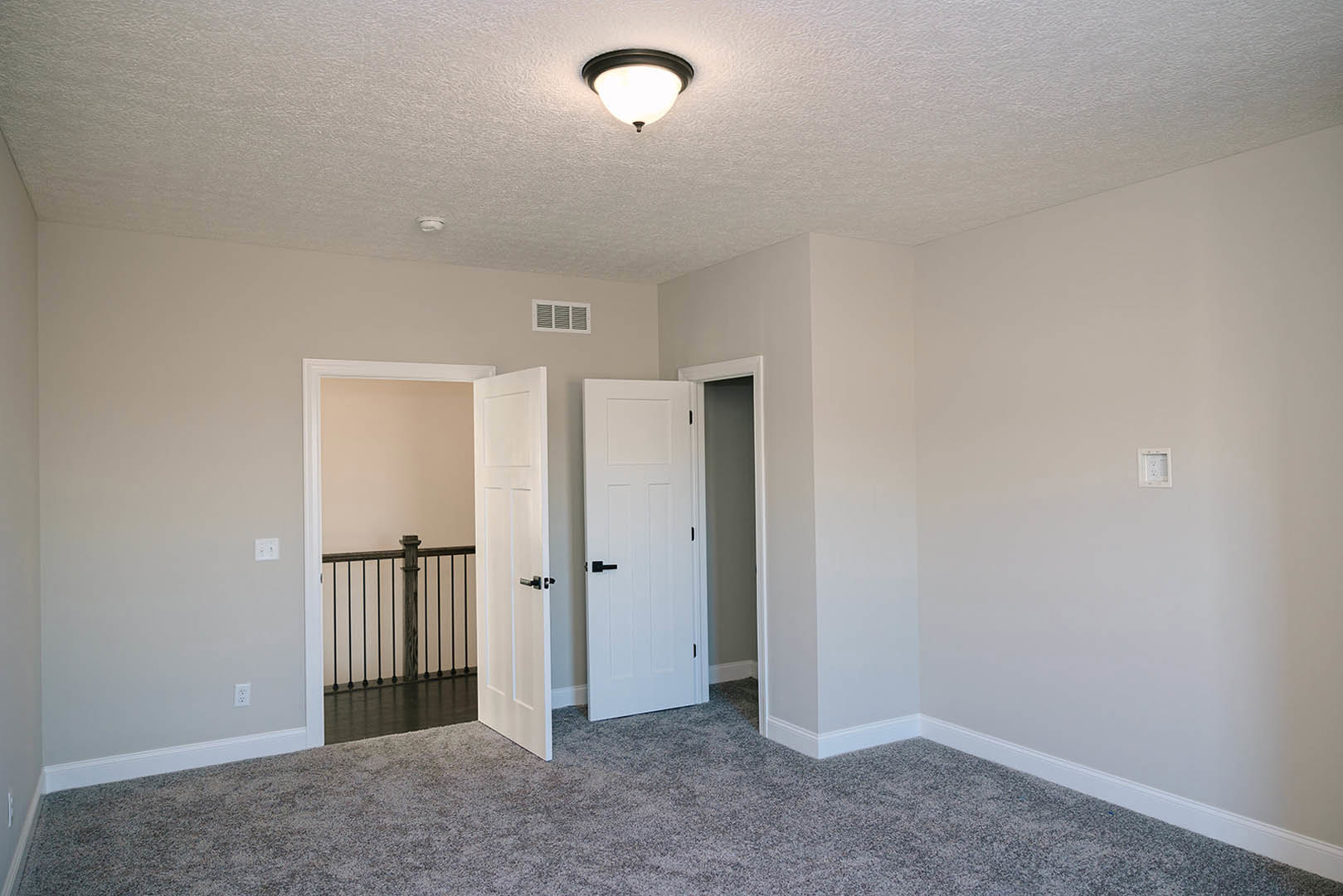 Neutral-toned room with two white doors featuring black handles, ceiling-mounted light fixture, carpeted floor, white-painted walls with molding, and a close-up view of a stair