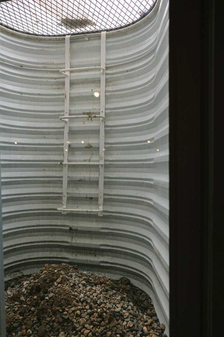 White metal ladder leaning against a steel water tank outdoors, with windows and building exterior visible in the background.