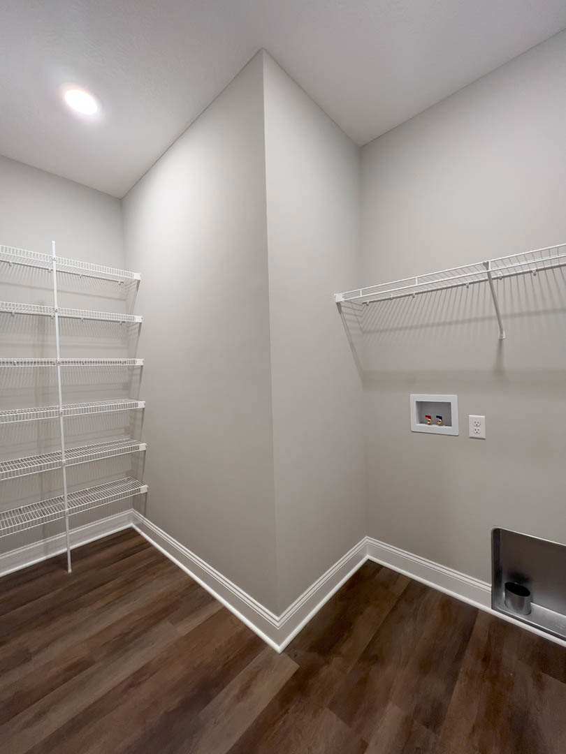 Corner room with white built-in shelves, wood flooring, white plaster walls, and metal can mounted on wall