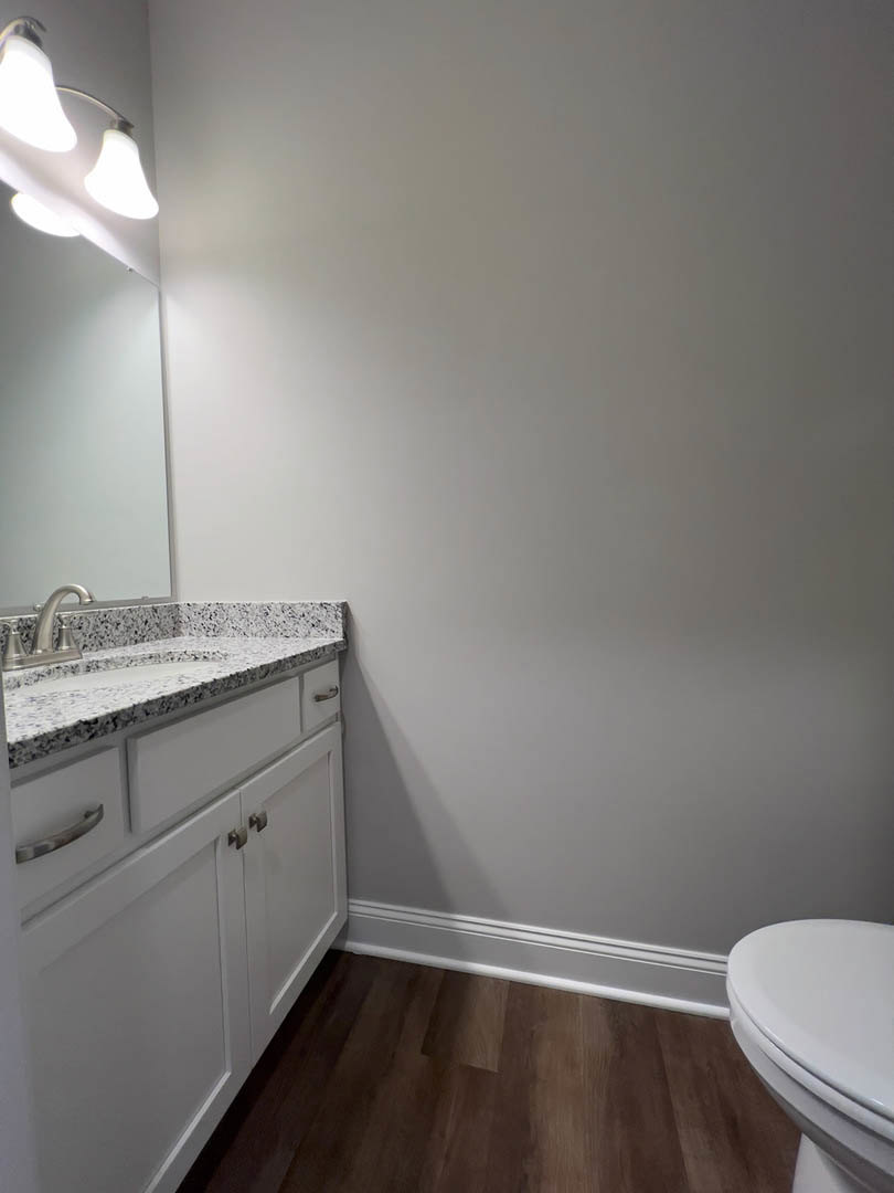 White porcelain sink and toilet set against light tile walls, dark wood flooring with white baseboards, chrome faucet, and wall-mounted light fixture.