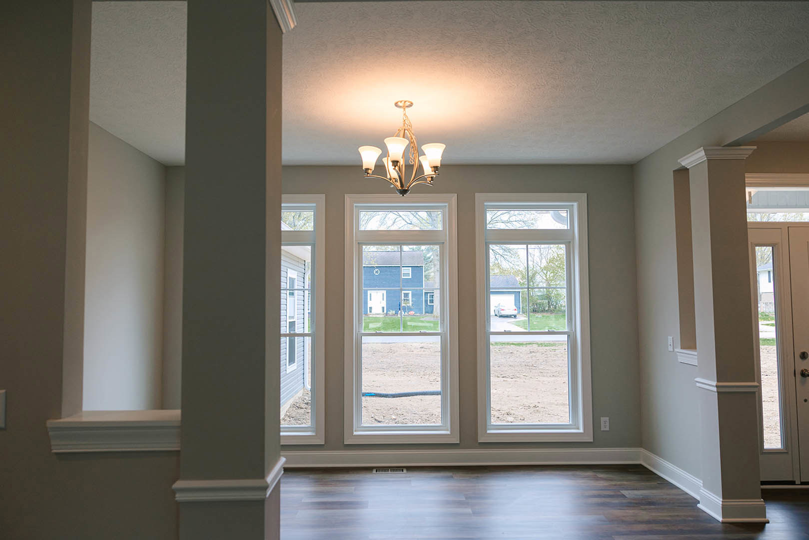 Chandelier hanging from ceiling in a room with two large windows, wood flooring, white walls, and decorative molding