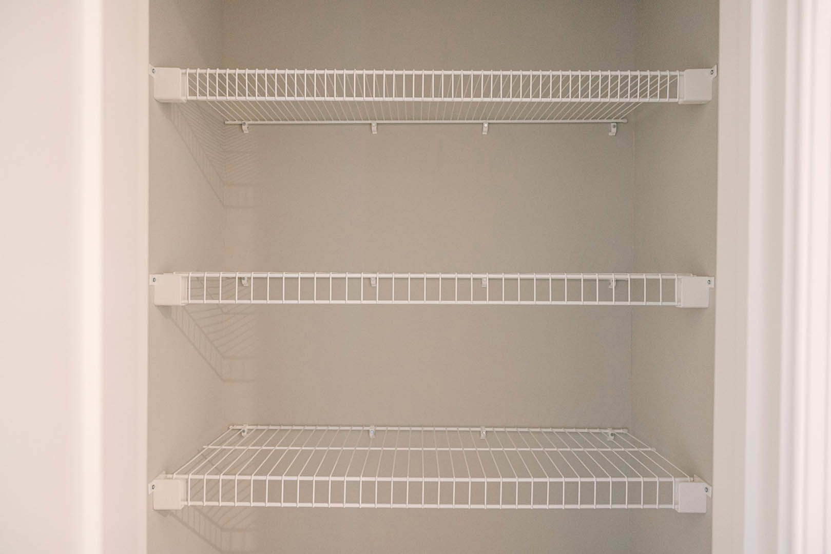 White wire shelf mounted on a white wall inside a closet, featuring a horizontal bar and perforated rack design.