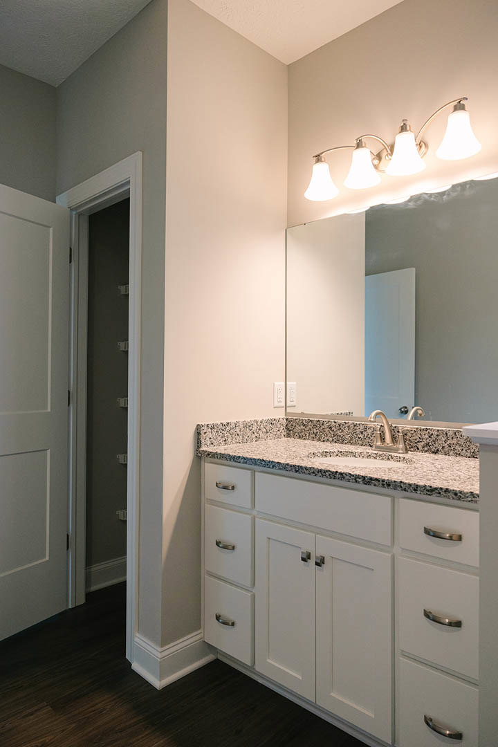 White bathroom vanity with marble countertop, under-mount sink, and drawers; large rectangular mirror above; white walls and door with black trim; modern light fixture mounted