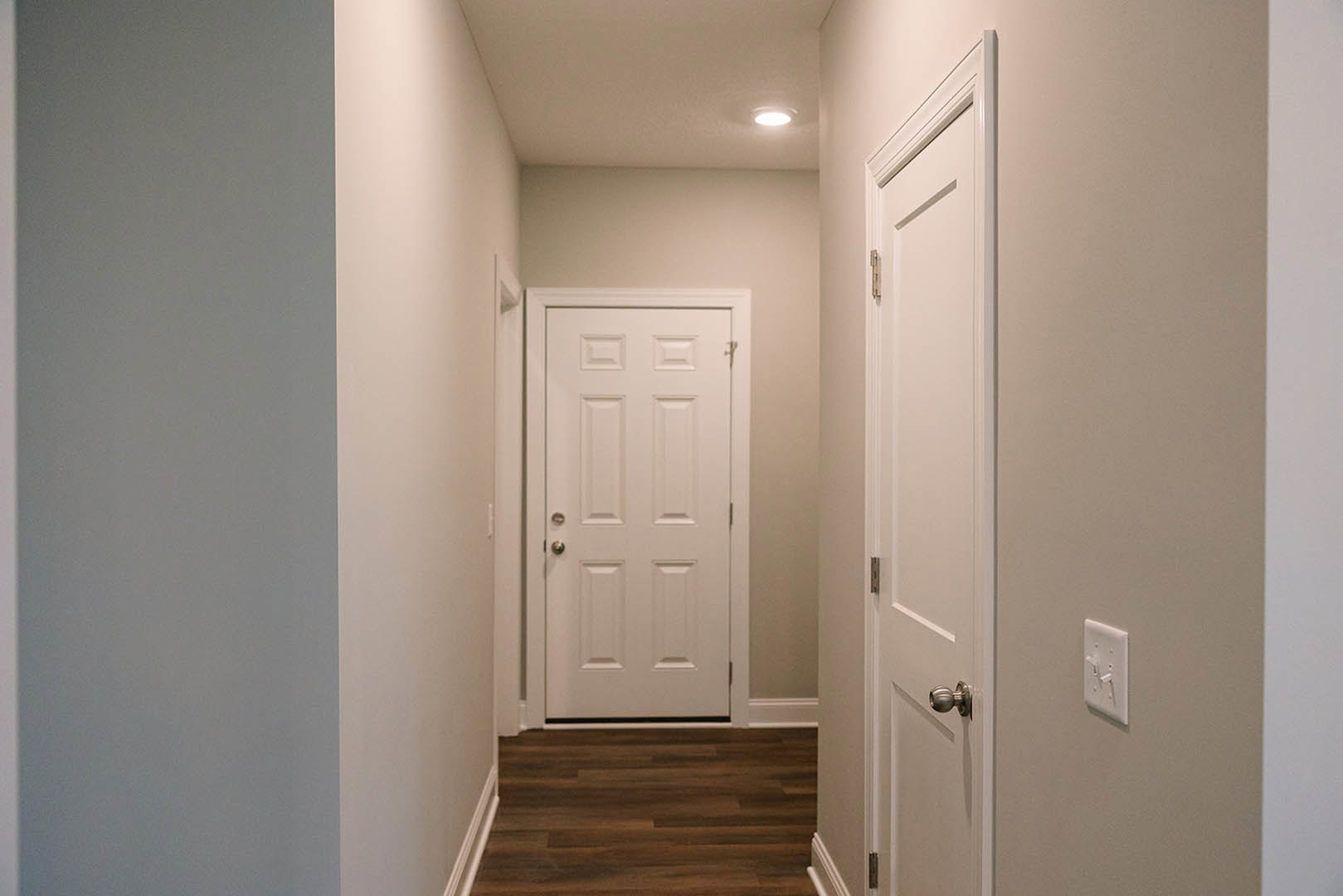 Hallway with white paneled doors, silver and black handles, wood flooring, white walls with trim, visible heater, and a close-up of a light switch