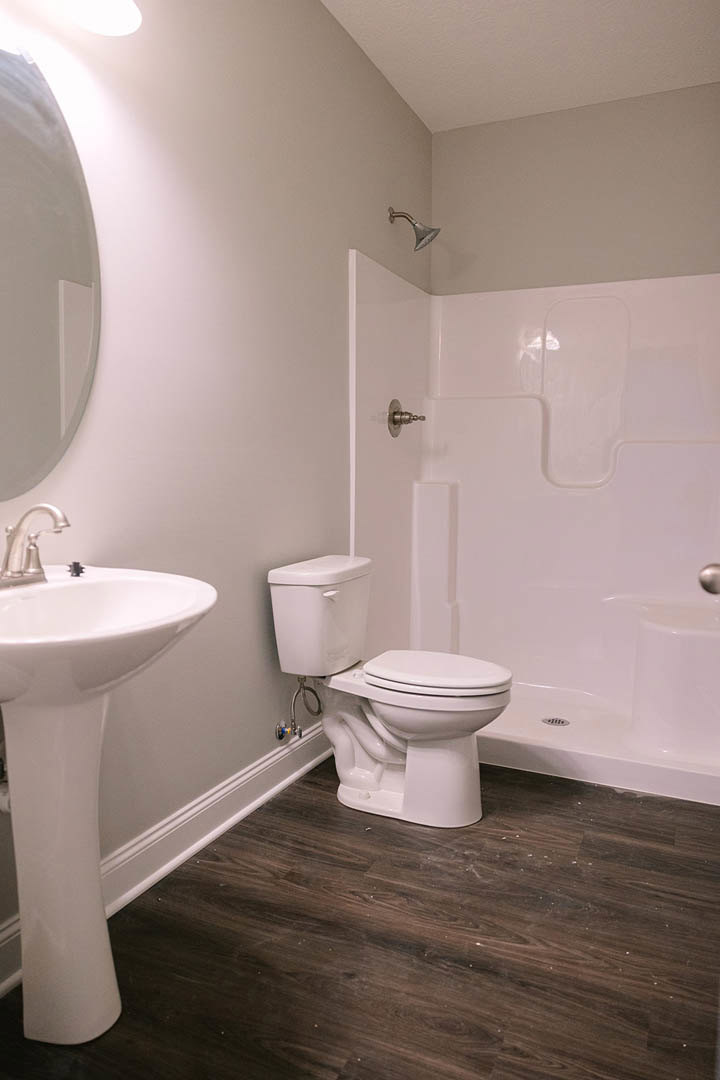 Modern bathroom featuring a white porcelain sink with chrome faucet, matching toilet, light wood flooring, large wall mirror, and neutral tile walls.