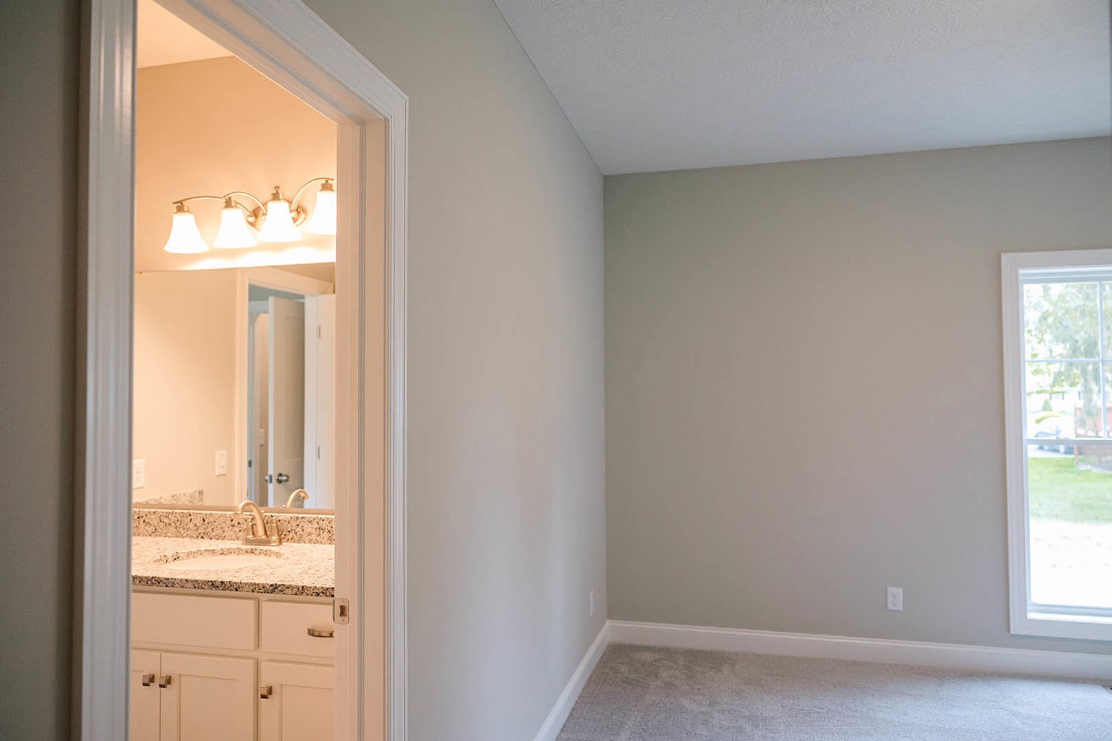 Bathroom featuring marble countertop with undermount sink, large mirror framed by wall-mounted lights, window overlooking grassy yard and trees, white cabinetry, plaster walls, and