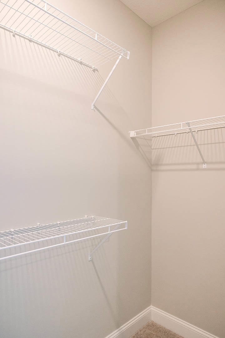 White wire shelving mounted on a white plaster wall above beige carpet in a laundry or bathroom space, with a white clothes dryer partially visible.