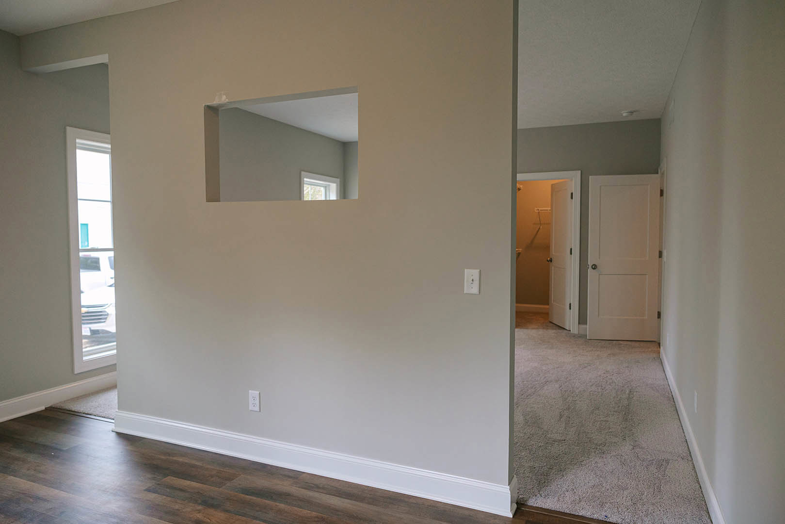 White paneled door set in a plaster wall with square window, wood laminate flooring, and white baseboard trim