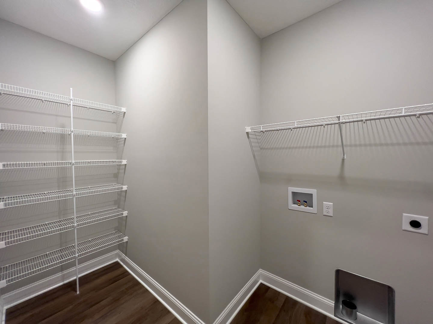 White built-in shelves along a plaster wall, wood plank flooring, recessed ceiling lighting, and a modern bathroom fixture with red and blue faucet handles.