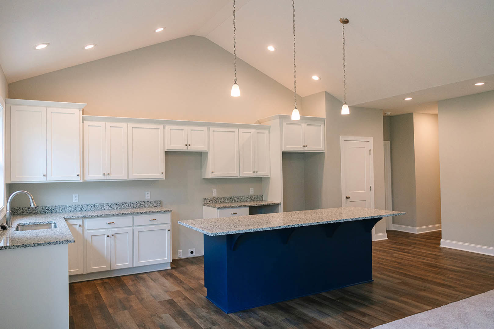 Blue kitchen island with marbled countertop, surrounded by white cabinets, black hardware, and white doors with black frames